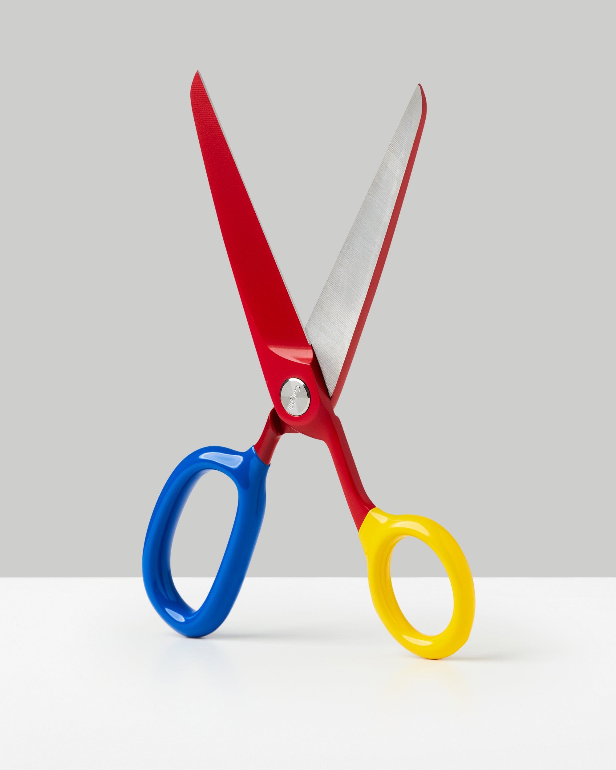 Craighill Chroma Scissors with red blades and blue and yellow handles, standing open against a gray background.